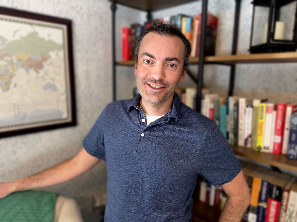 Rob Howard smiling indoors beside bookshelves and a framed world map.